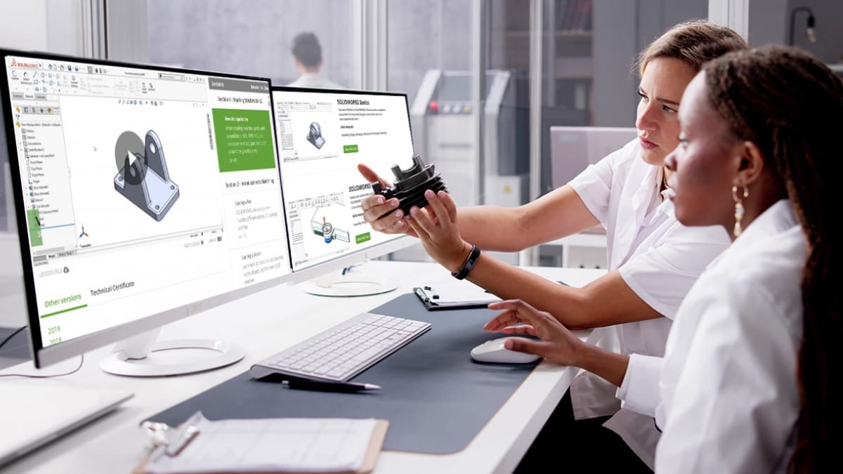 Two engineers reviewing a manufactured part while following a SolidProfessor SOLIDWORKS training course on dual monitors.